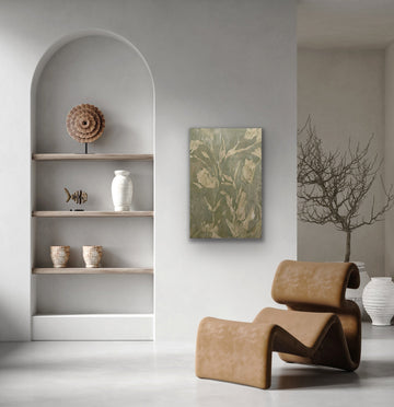 “Sage green and cream abstract botanical painting displayed beside arched shelves and a sculptural brown chair in a neutral interior.”